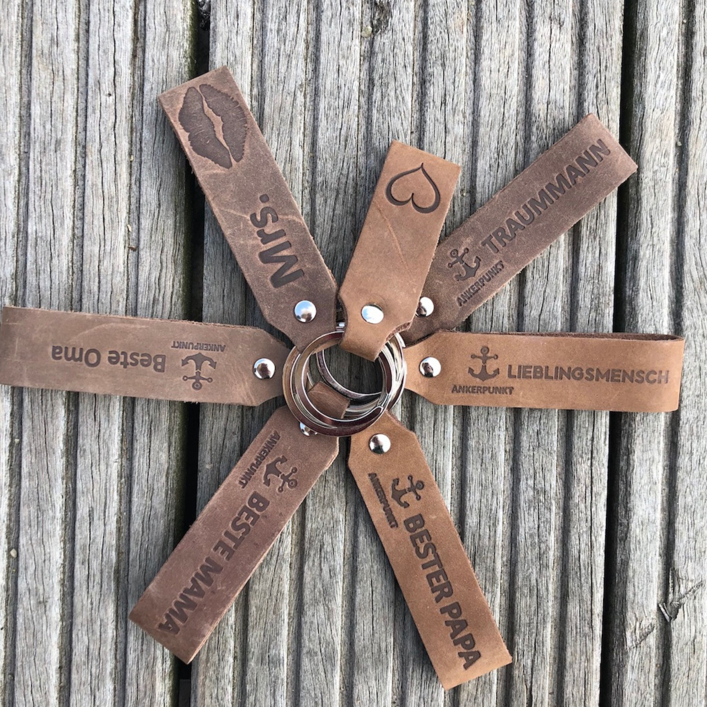 Sieben Schlüsselanhänger liegen mit dem Ringende aneinander auf einer Holzbohle.