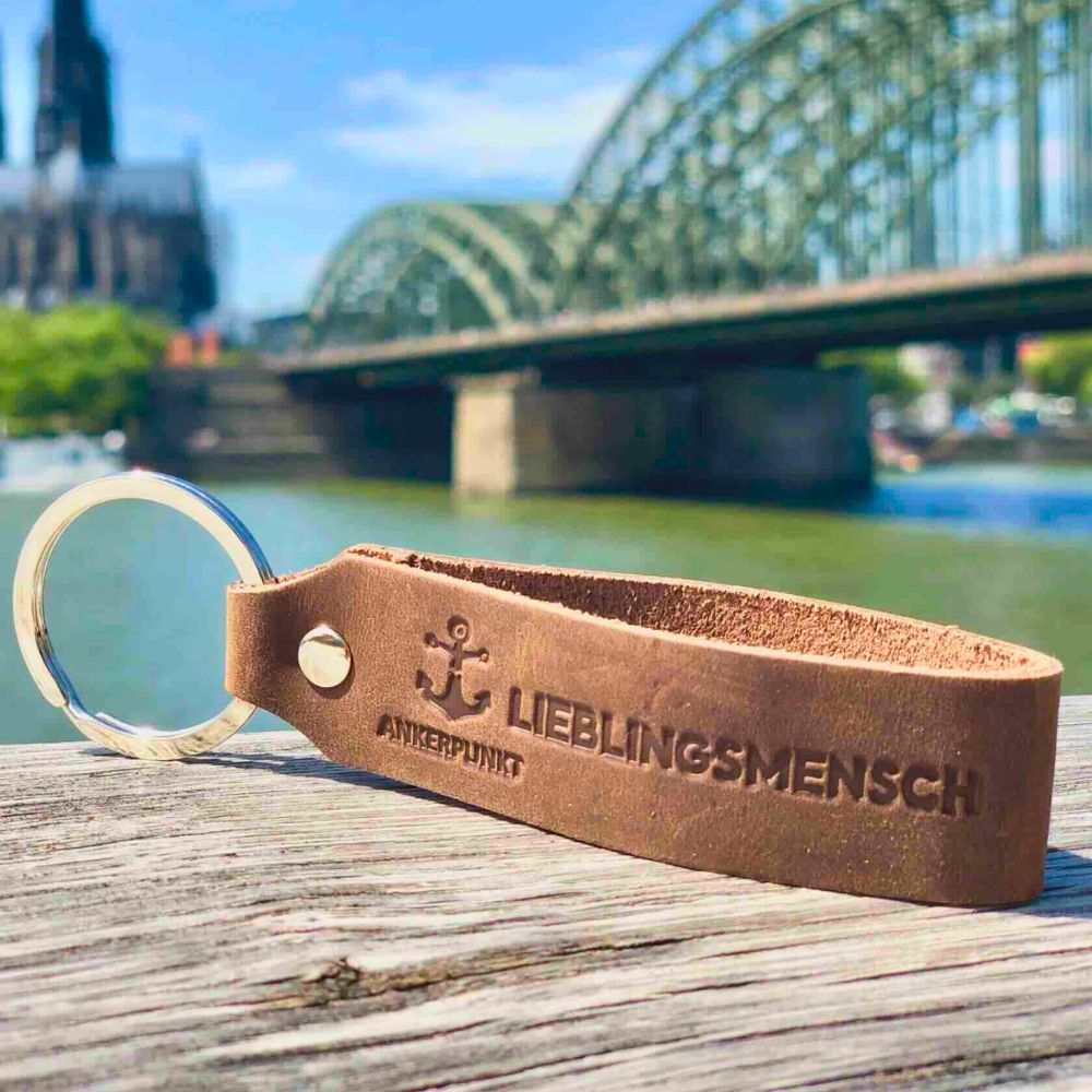 ANKERPUNKT Schlüsselanhänger aus Leder mit Gravur "Lieblingsmensch" vor Brückenhintergrund.