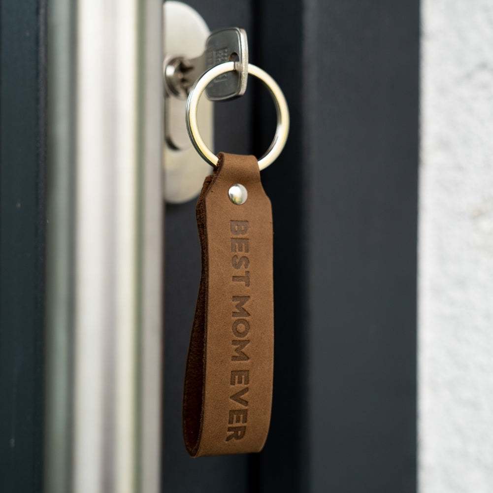 Dark brown leather keychain with "Best Mom Ever" engraving hanging from a key in a door lock; ANKERPUNKT quality German craftsmanship.
