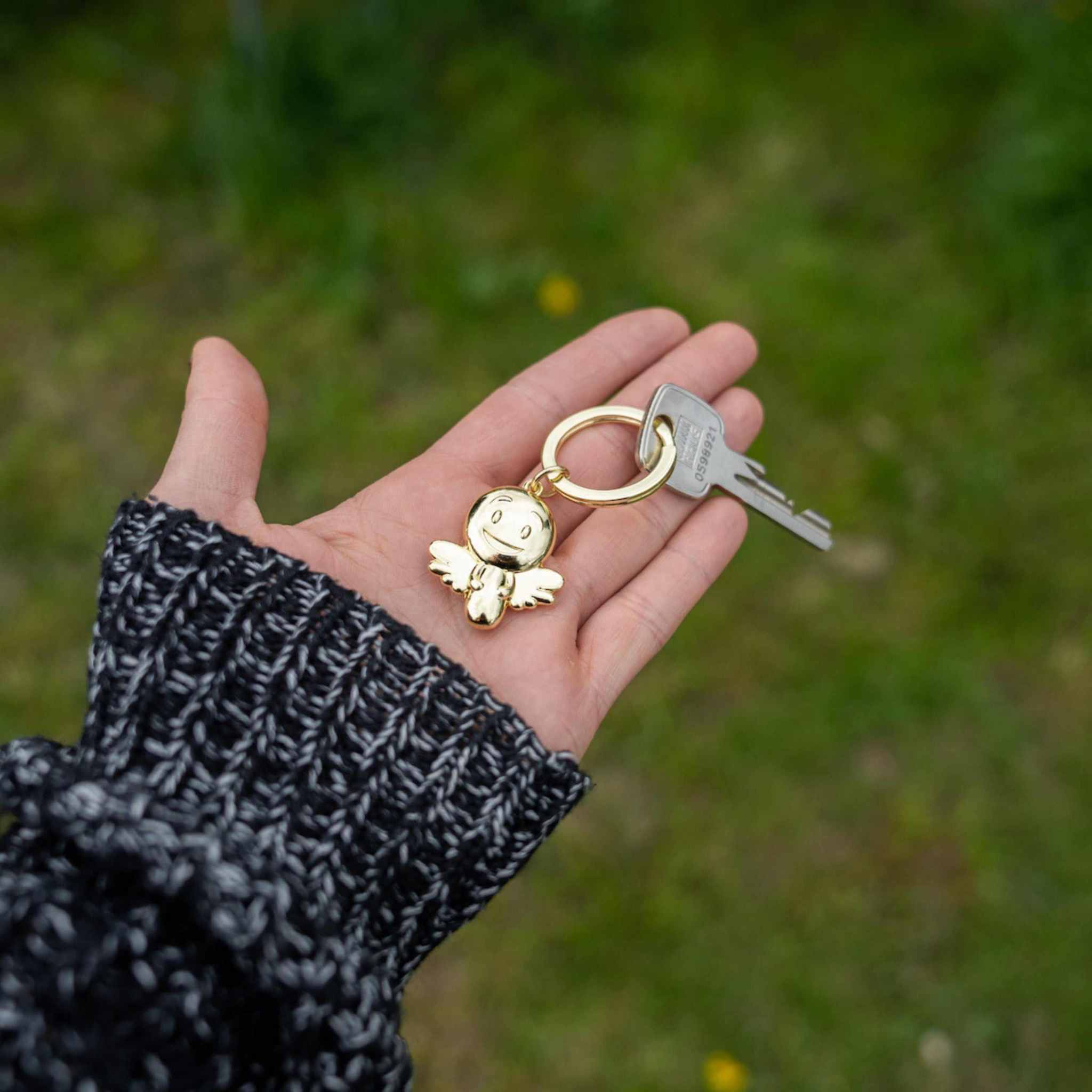 Gold glänzender Schutzengel Schlüsselanhänger mit Smiley in der Hand.