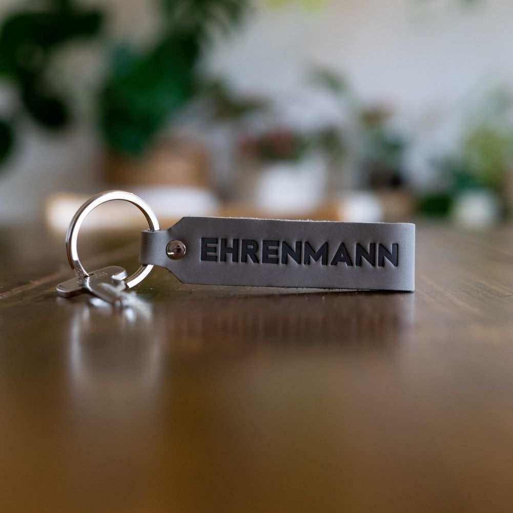 Gray leather keychain set "Ehrenmann & Ehrenfrau" on wooden surface.