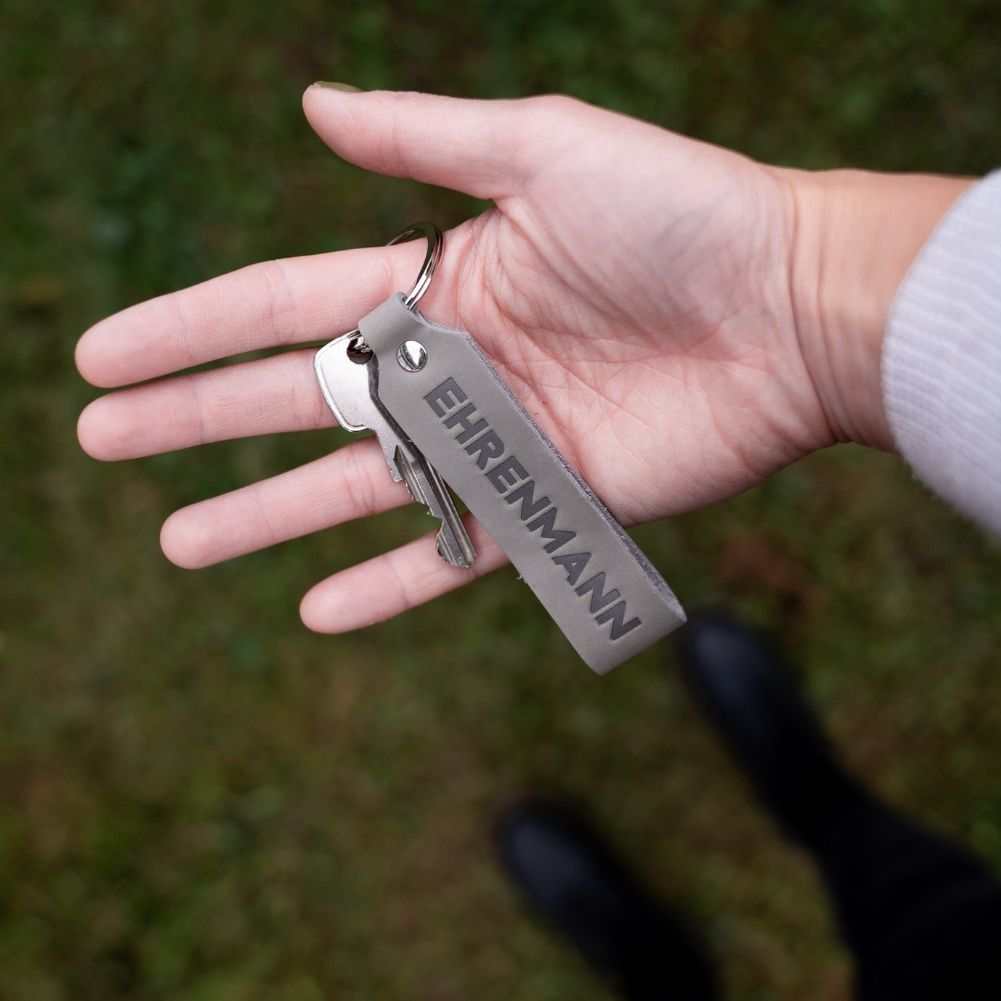 Gray leather keychain set with "Ehrenmann" engraving held in hand, perfect gift for couples.