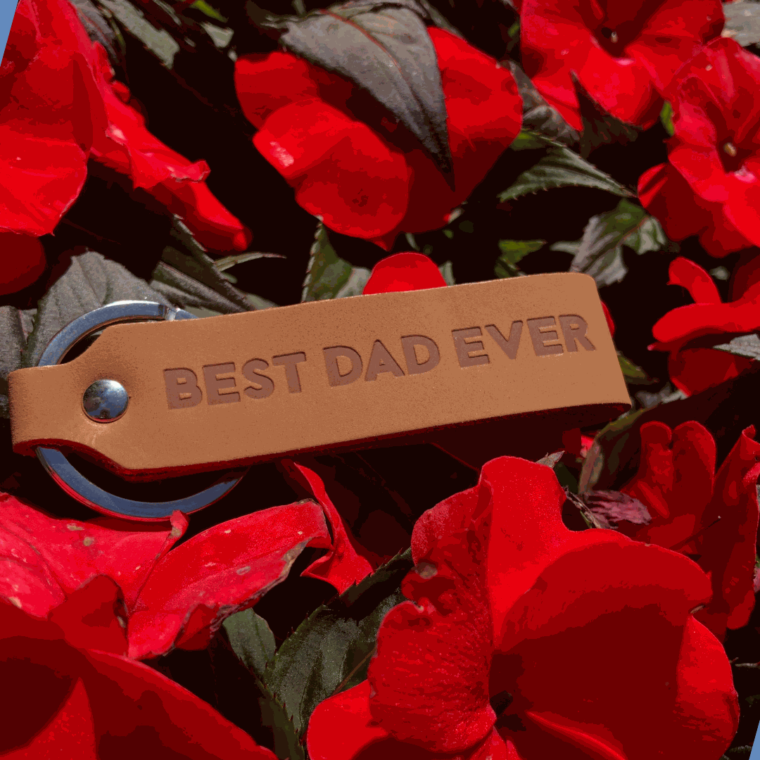 Light brown leather keychain engraved with "Best Dad Ever" amidst vibrant red flowers.