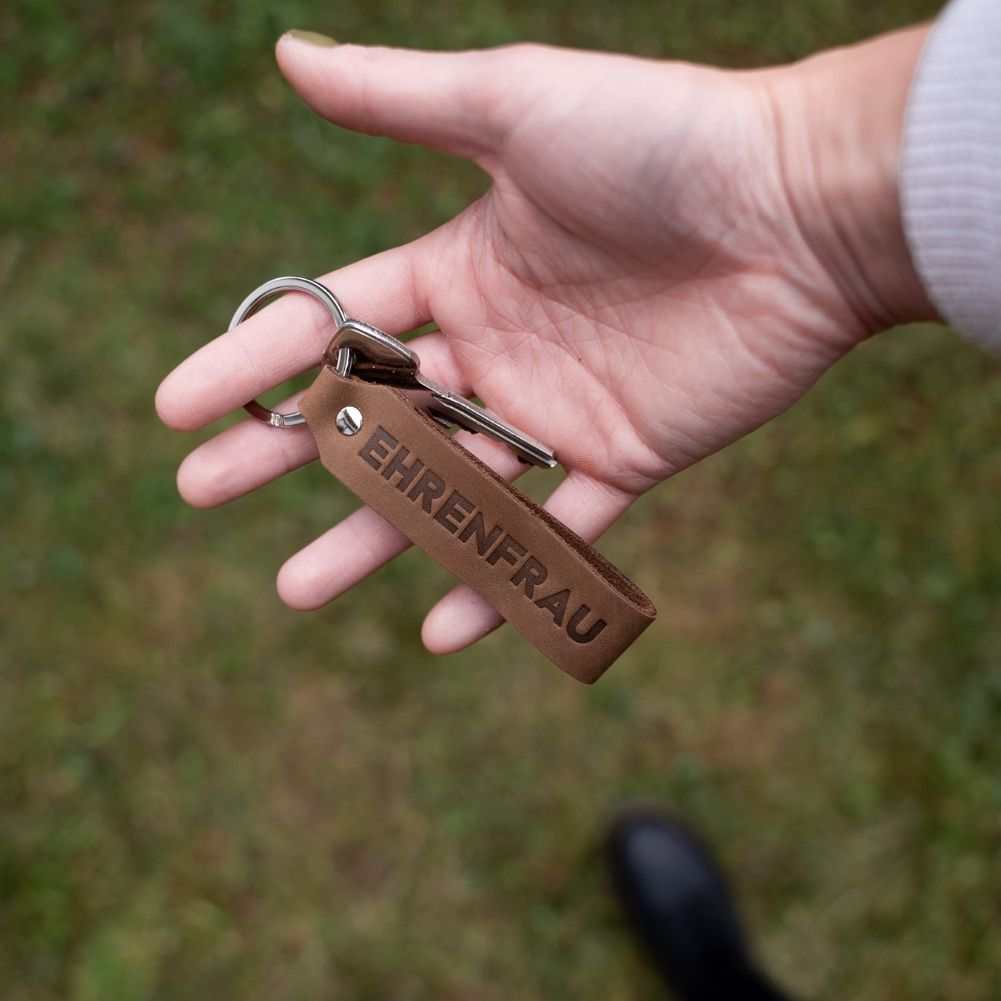 Dunkelbrauner ANKERPUNKT Schlüsselanhänger aus Leder mit Gravur "EHRENFRAU" in Hand gehalten.