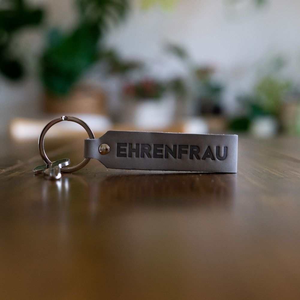 ANKERPUNKT Schlüsselanhänger Leder mit Gravur Ehrenfrau in Grau auf Tisch.