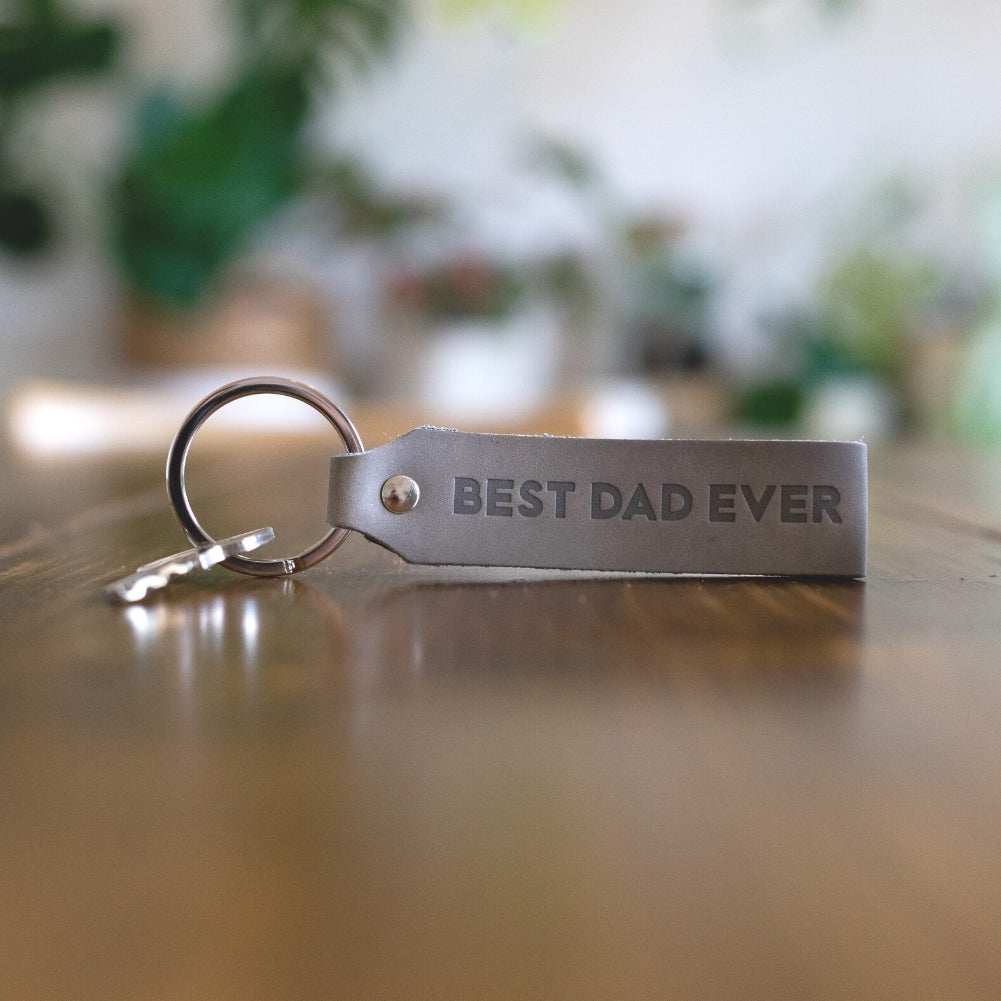 Schlüsselanhänger Leder Best Dad Ever grau auf Holztisch.