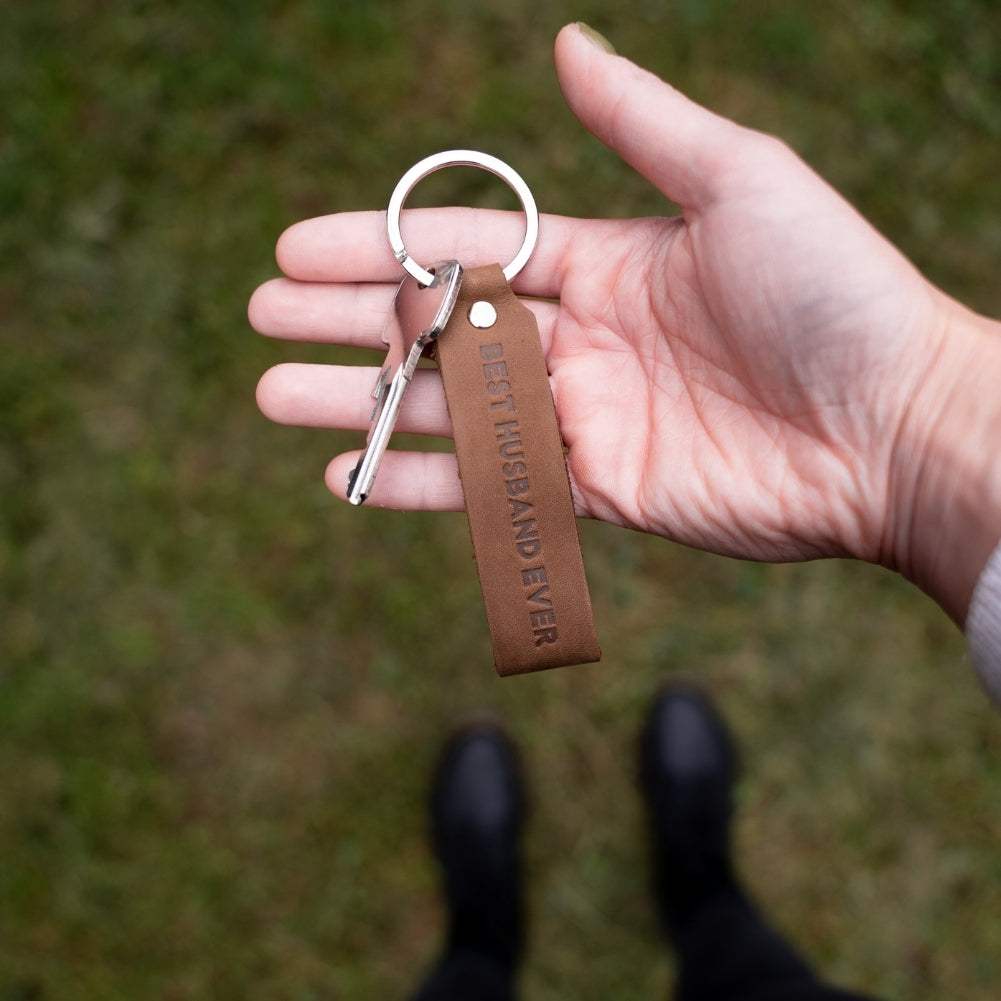 Dark brown ANKERPUNKT leather keychain with "Best Husband Ever" engraving, held in hand.