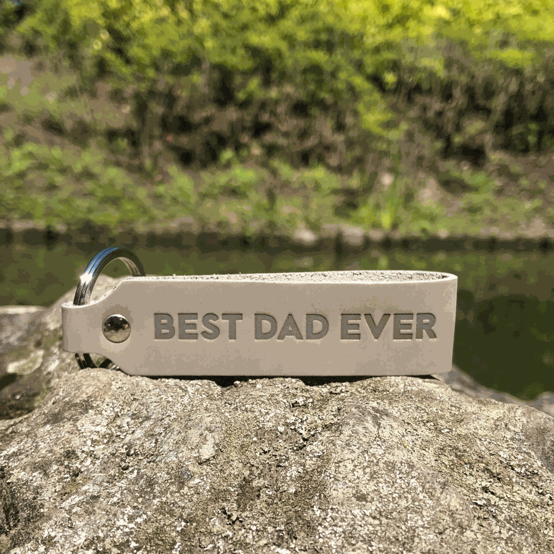 Schlüsselanhänger Leder mit Gravur "Best Dad Ever" in Grau auf Steinoberfläche.