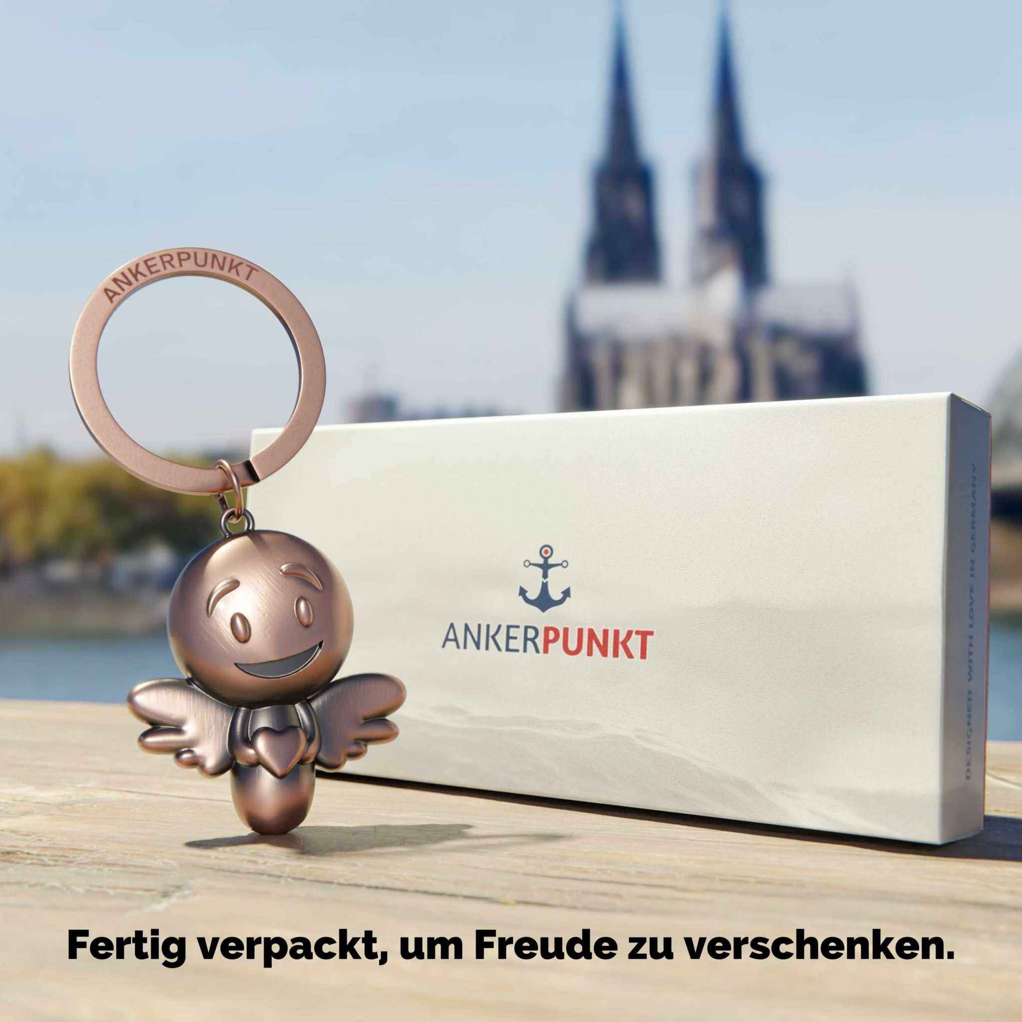 Schutzengel Schlüsselanhänger aus Bronze vor Geschenkverpackung mit Dom-Hintergrund.