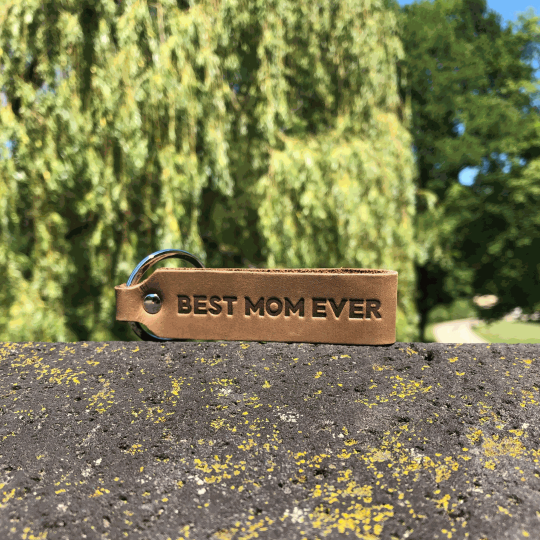 ANKERPUNKT Schlüsselanhänger "Best Mom Ever" aus dunkelbraunem Leder auf Steinwand.