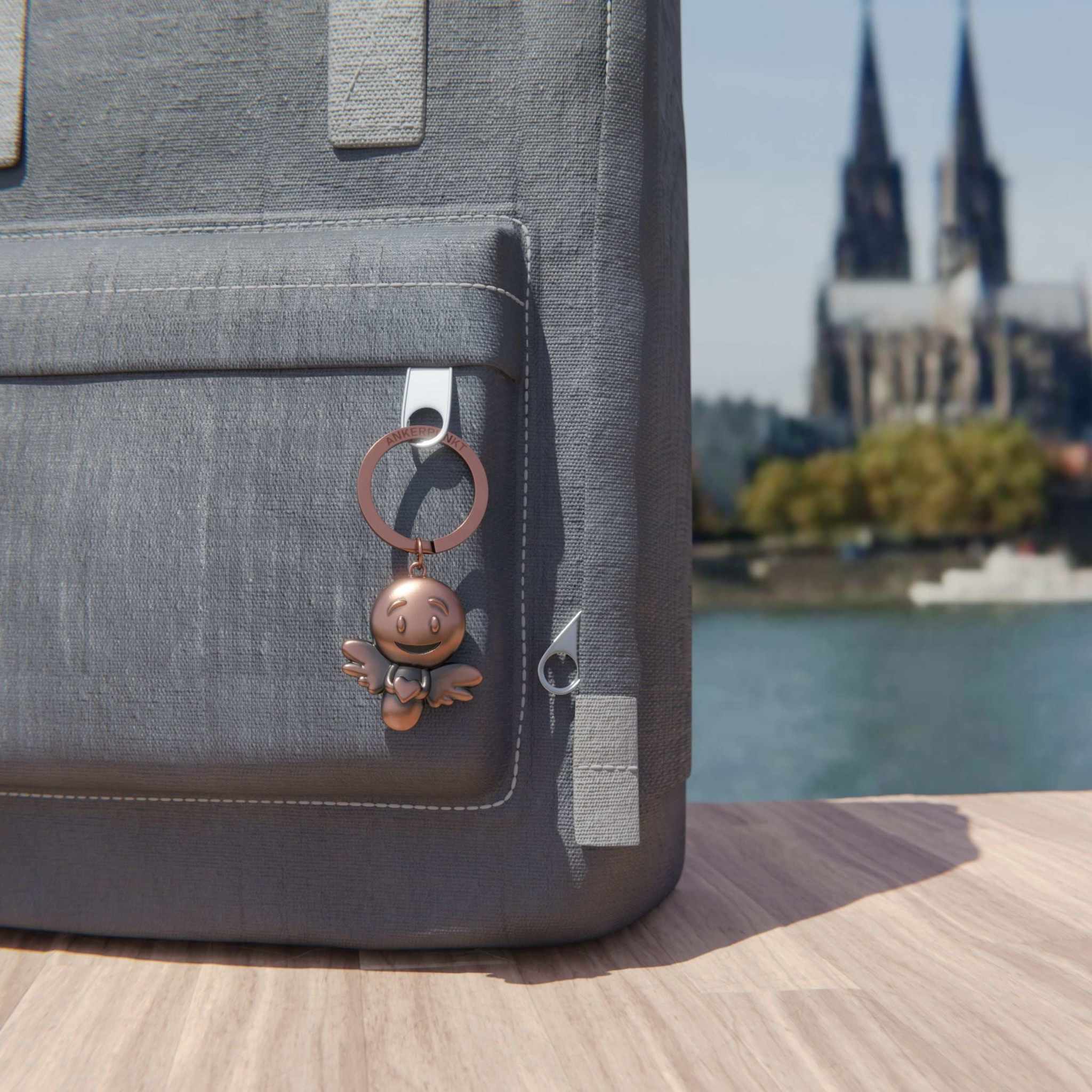 Bronze vintage Schutzengel Schlüsselanhänger on a gray backpack with cathedral view.